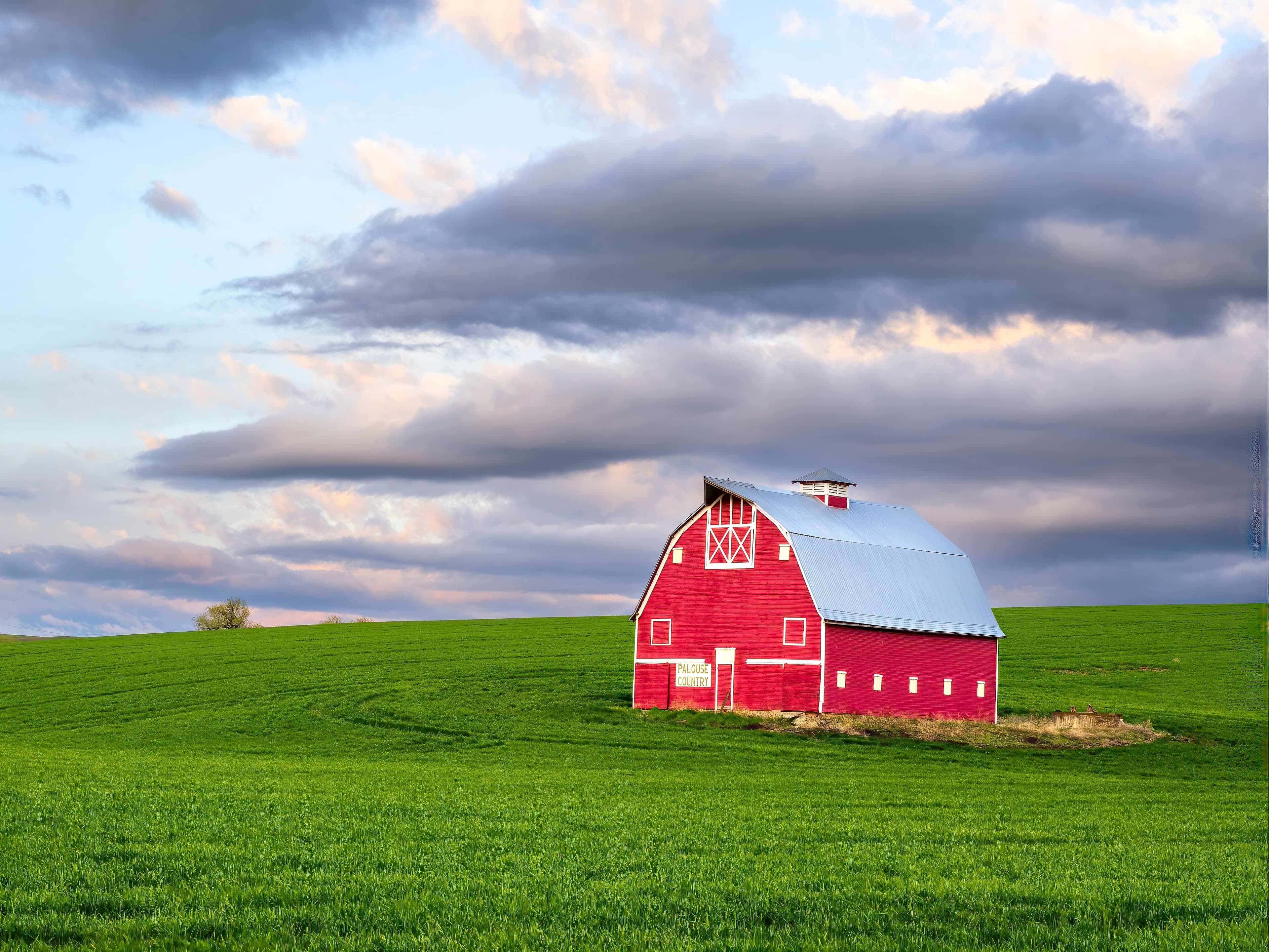 Iconic red barn perched on a green hillside beneath dramatic spring clouds in Palouse, Washington